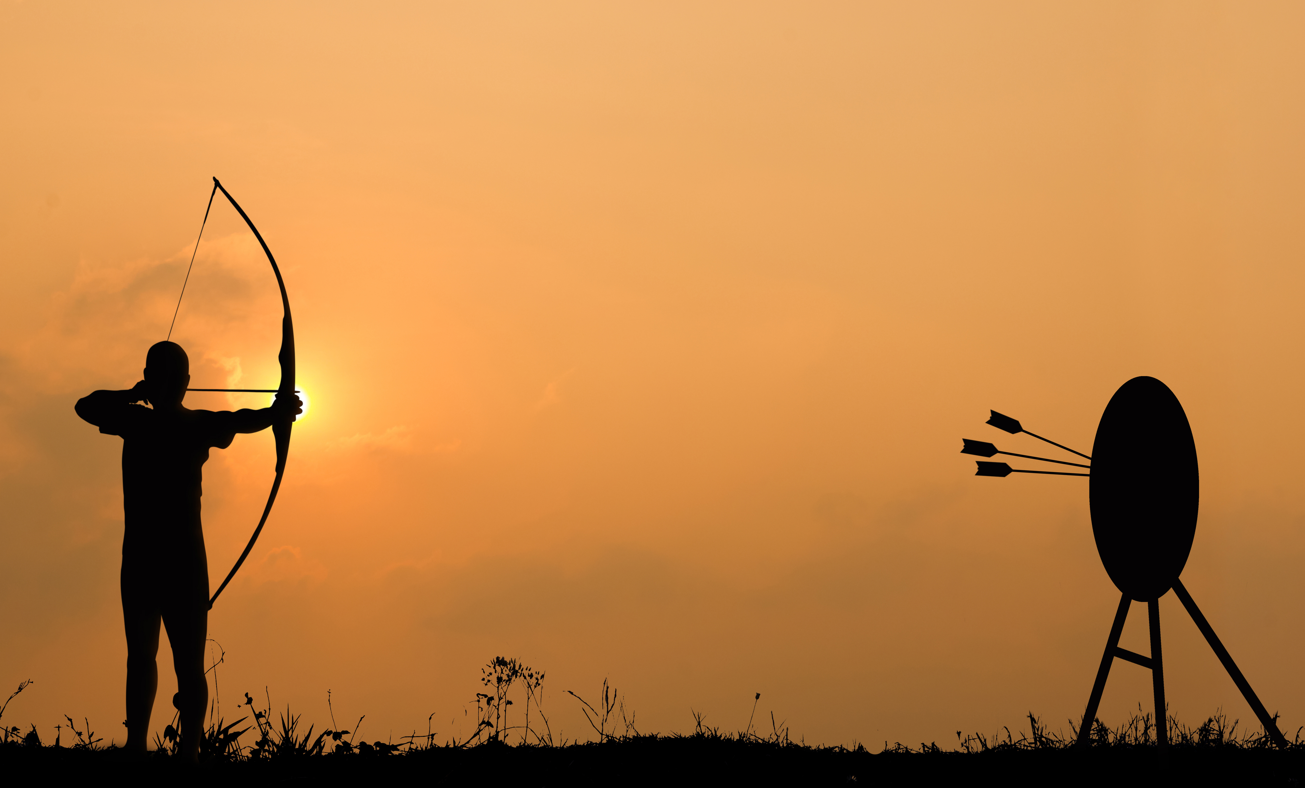 Silhouette of a person shooting a bow and arrow at dusk